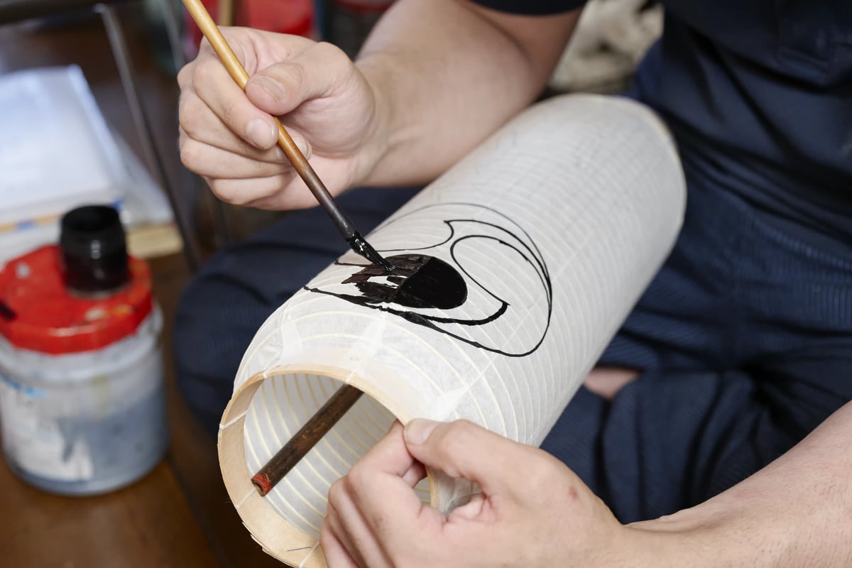 A brush laying down the black outline of a crest on a lantern