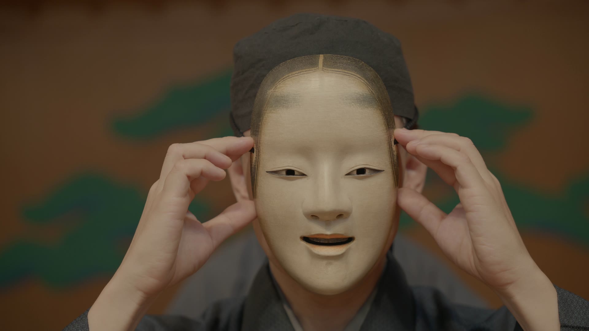 A carved Noh mask being settled onto a performer's face